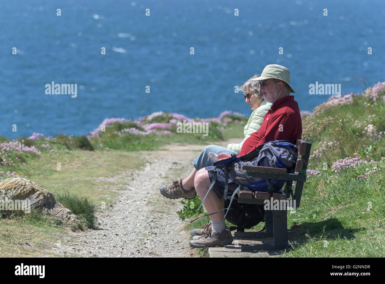Beau temps comme deux marcheurs profitez d'un repos sur un banc sur le Pointe Pentire à Newquay, Cornwall. Banque D'Images
