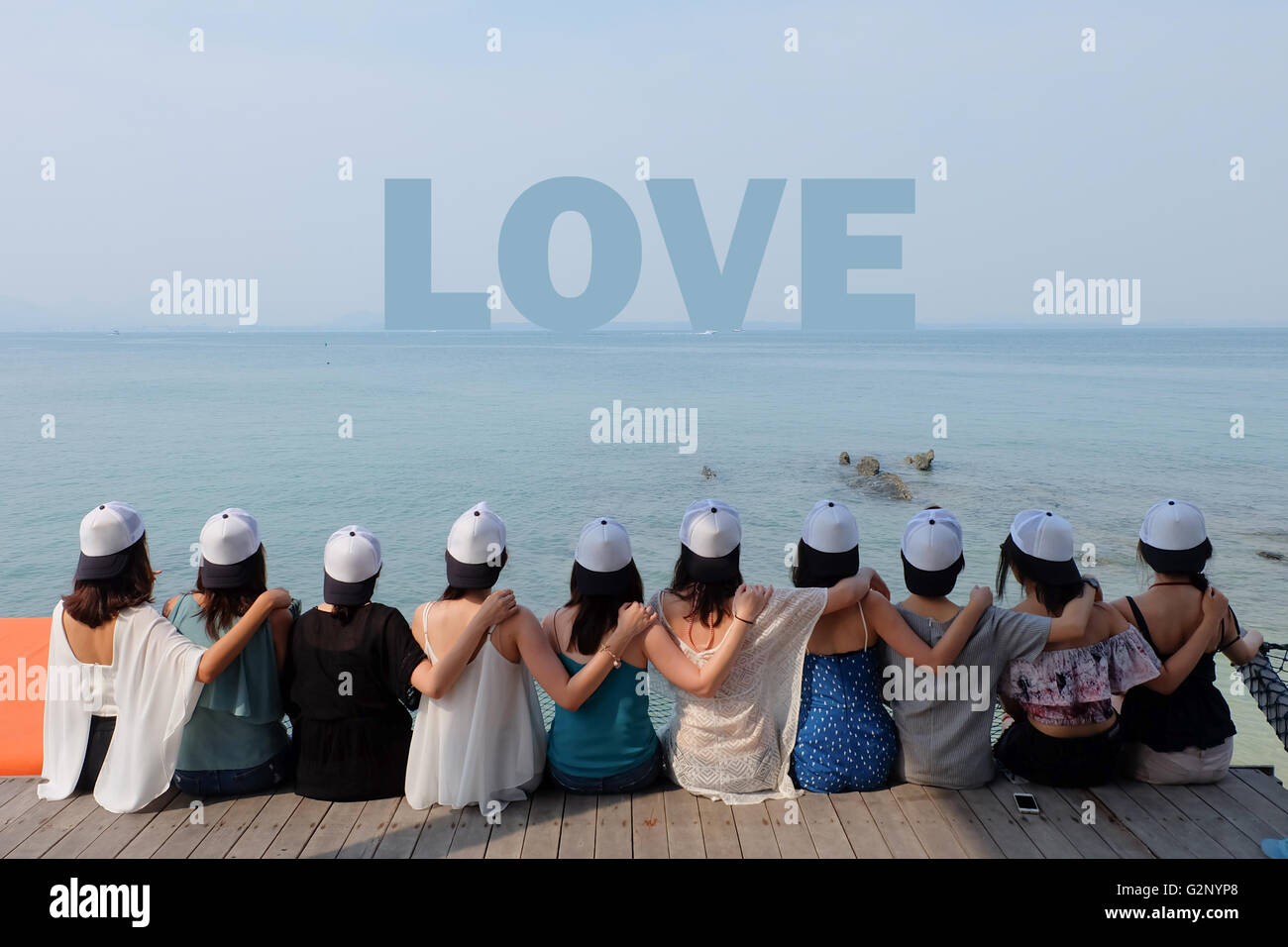 Groupe de dix femmes amis s'asseoir ensemble chercher amour hug mer ciel bleu. Banque D'Images