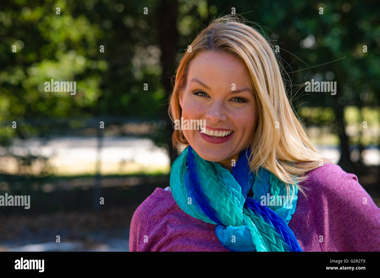 Portrait of smiling blonde woman en violet avec écharpe bleue à l'extérieur Banque D'Images