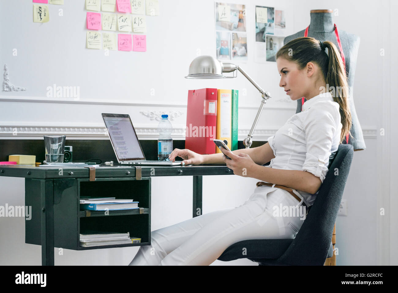 Une jeune femme est assise sur le côté d'affaires à son bureau dans son espace créatif à la recherche à son ordinateur portable Banque D'Images