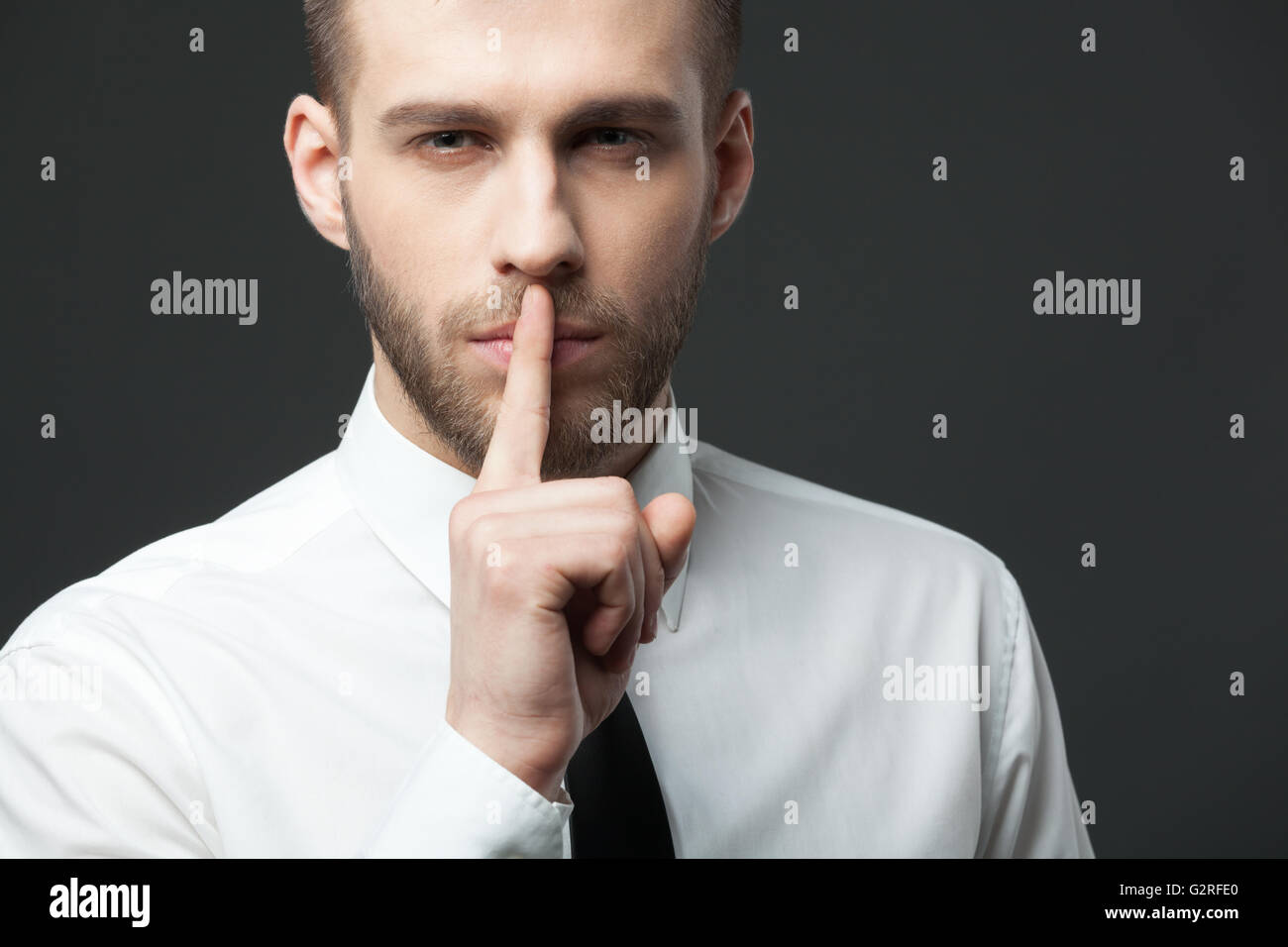 Gardez vos secrets ! Young handsome businessman gesturing 'shh' pour l'appareil photo. Banque D'Images