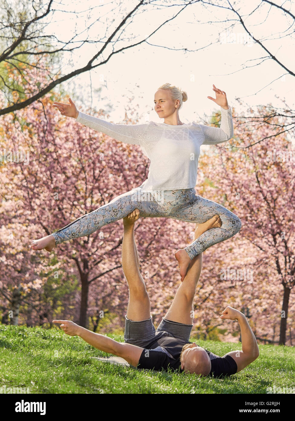 Formation Couple yoga acro dans un parc, les fleurs de cerisier sur arrière-plan, en mai au sud de la Finlande. Banque D'Images