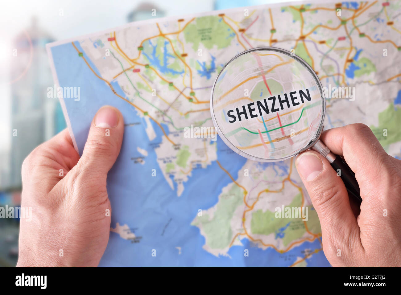 Mains de ramasser une carte de Shenzhen et à un emplacement avec une loupe avec monument représentant Banque D'Images
