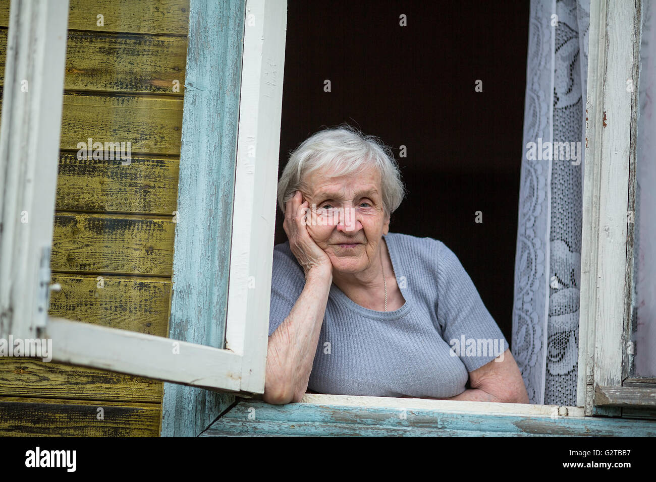 Une femme âgée (80 ans) assis et regarder par la fenêtre. Banque D'Images