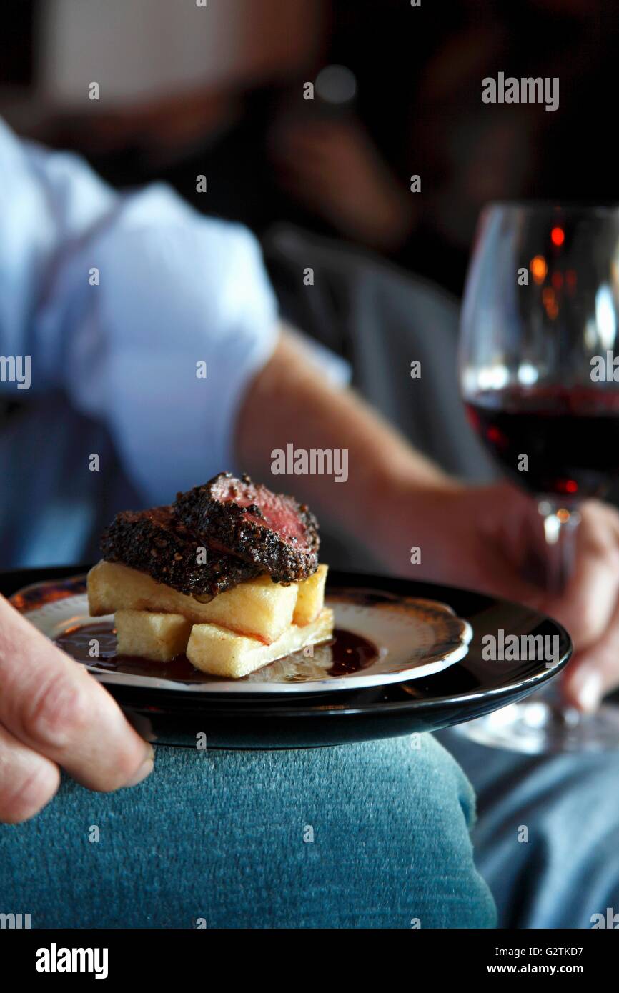 Un homme tenant une assiette de steak d'autruche et de chips et un verre de vin rouge Banque D'Images