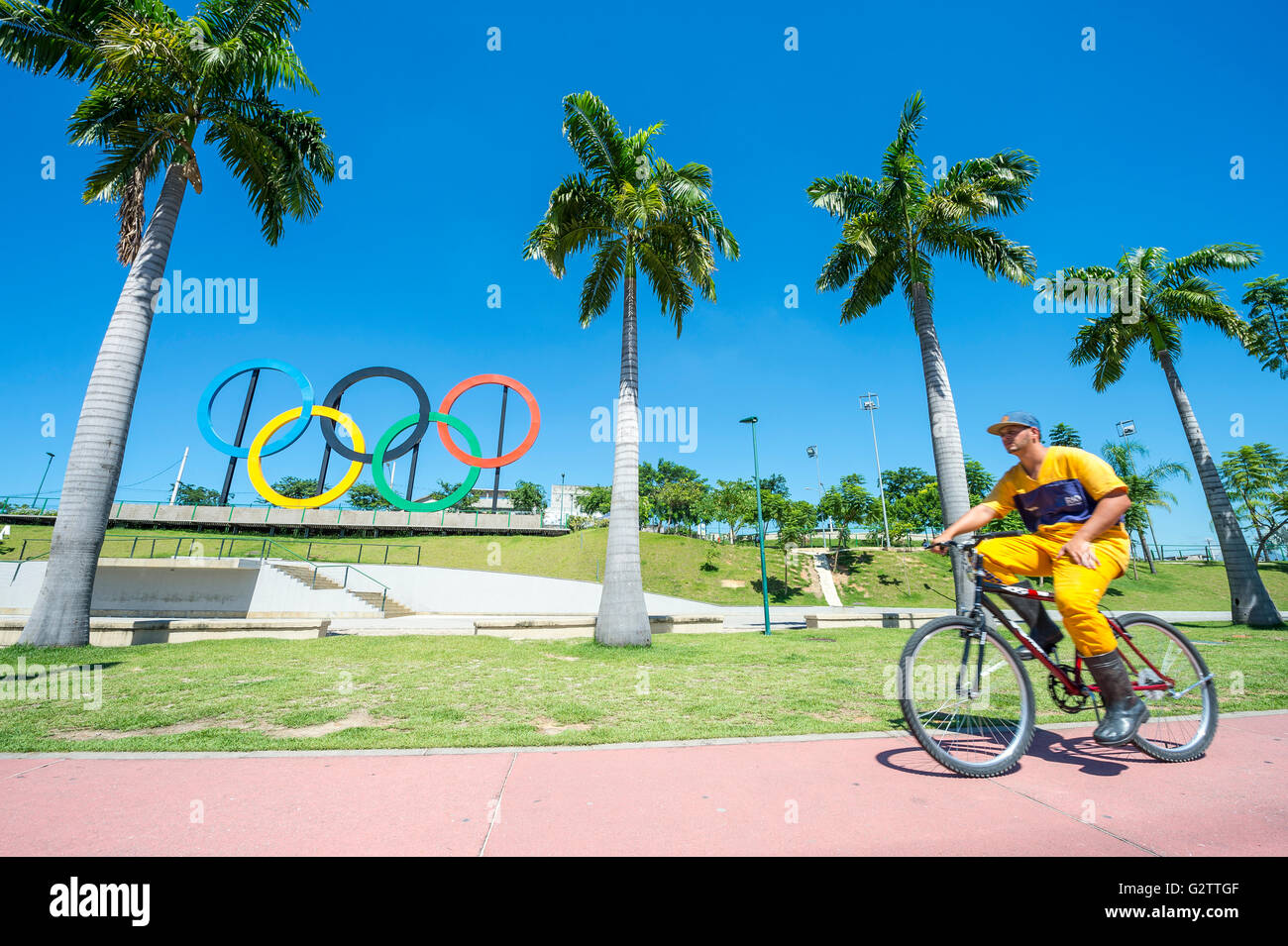 RIO DE JANEIRO - le 18 mars 2016 : un travailleur pour la COMLURB, entreprise de nettoyage municipal, conduit une bicyclette en face d'Anneaux olympiques Banque D'Images
