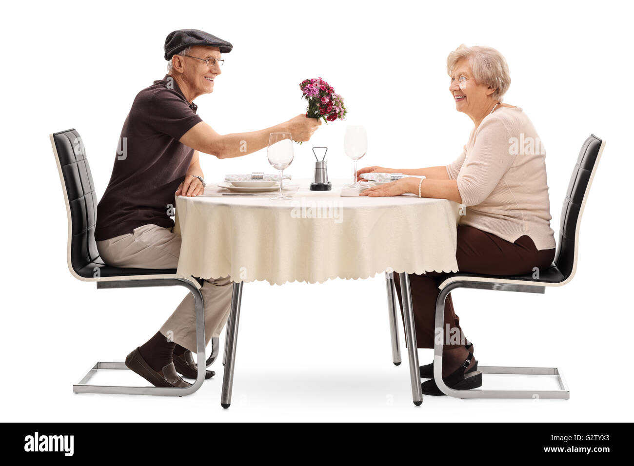 Homme mature donnant des fleurs à sa femme assis sur une date à une table isolé sur fond blanc Banque D'Images