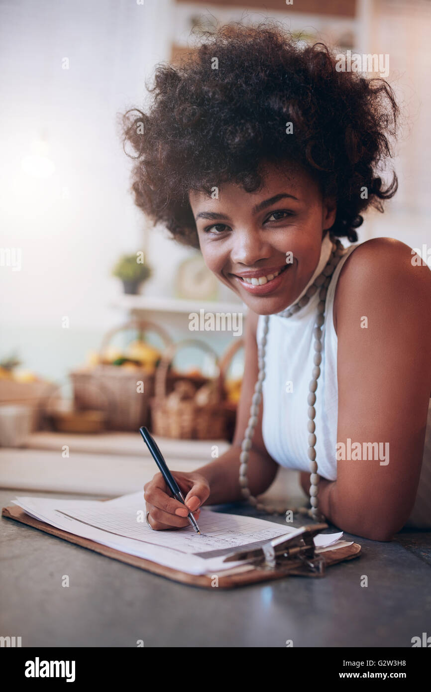 Portrait de jeune femme travaillant dans un bar à jus et à écrire des notes. Femme africaine debout derrière le comptoir à la recherche à Banque D'Images