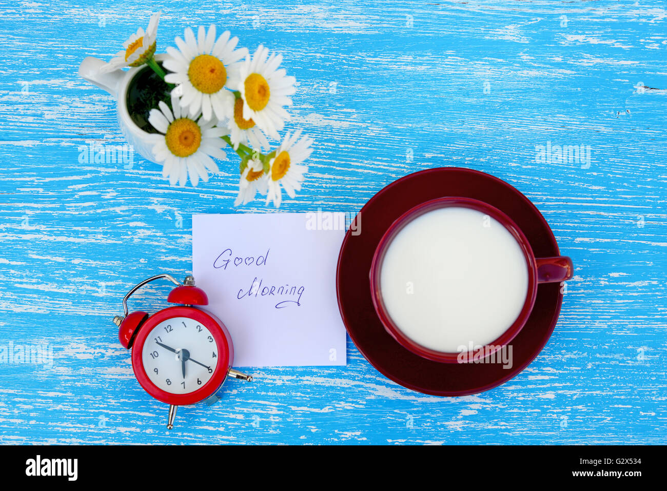 Fleurs Daisy et tasse de lait avec un bon matin note sur fond de bois bleu rustique Banque D'Images