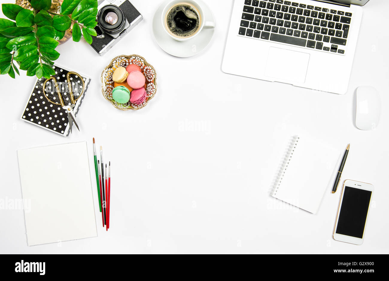 Creative home office du travail. Macaron café, gâteaux, ordinateur portable et plante verte sur fond de table blanc. Mise à plat Banque D'Images