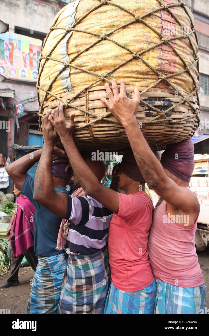 Quatre travailleurs transportant une lourde panier contenant des légumes dans un marché à Kolkata Banque D'Images