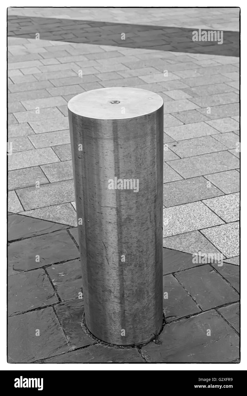 Photo en noir et blanc d'un bollard gris acier inoxydable sur chaussée avec quelques lignes de dalles gris foncé avec un vintage bo Banque D'Images