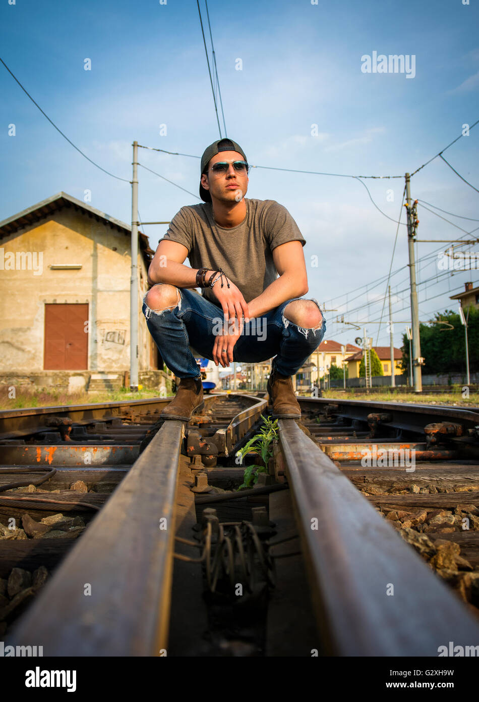 Young man sitting on Railroad, le port de t-shirt gris et un jean, à l'écart Banque D'Images