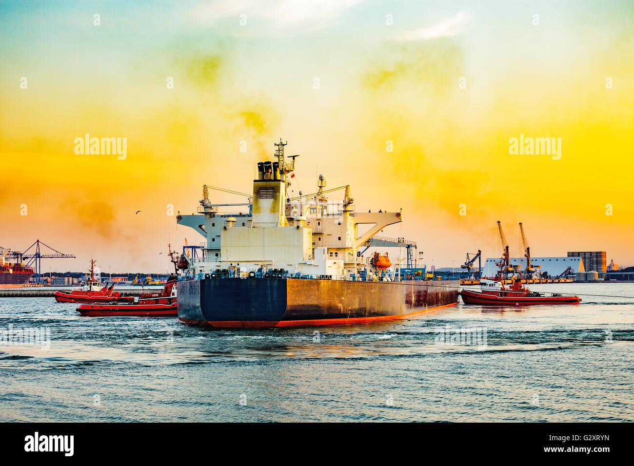 Grand navire d'escorter des remorqueurs de quitter le port au coucher du soleil. Banque D'Images