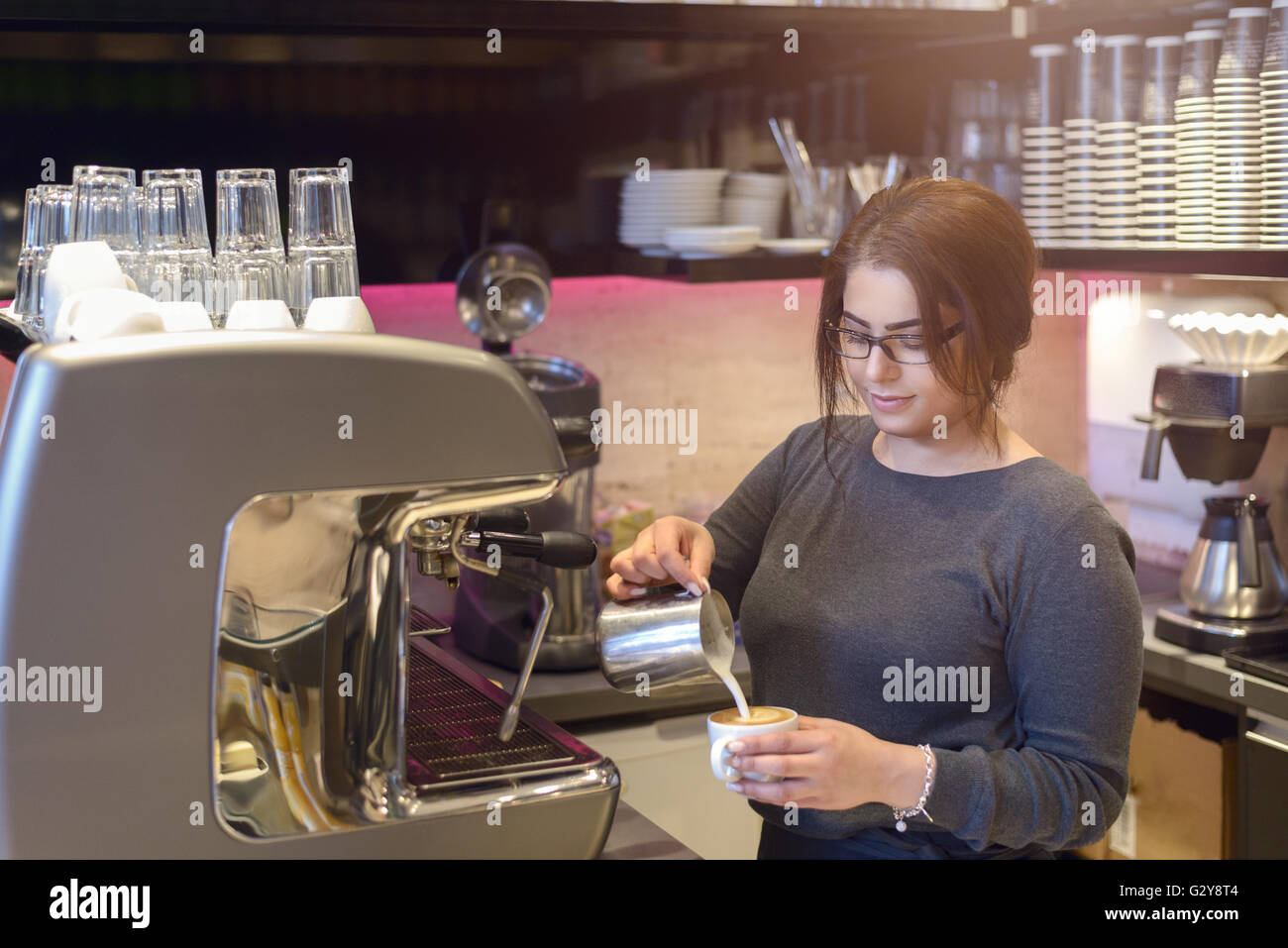 Barista femelle ou une serveuse de prendre une tasse de cappuccino dans un café ou d'une cafétéria de verser le lait moussé chaud dans le café Banque D'Images