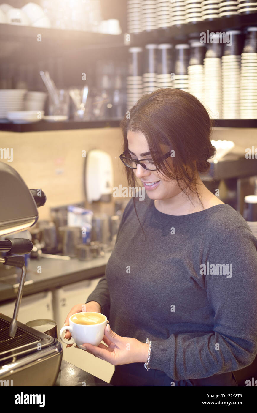Female barista ou waitress holding une tasse de cappuccino dans un café ou d'une cafétéria, souriant montrant satisfaction Banque D'Images