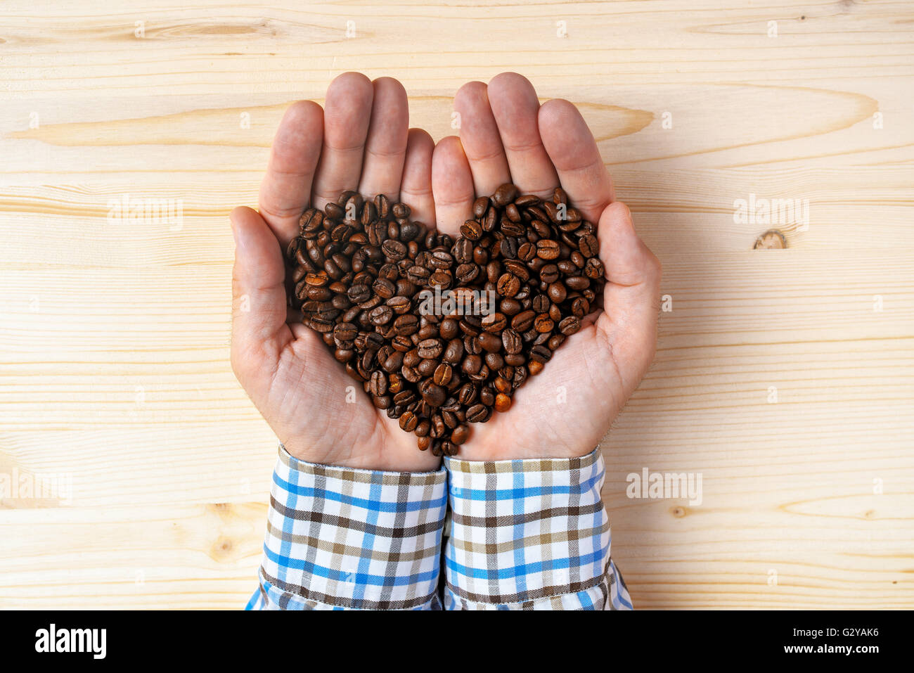 Poignée de grains de café torréfiés tas en forme de coeur, vue du dessus de l'homme de main au cours d'un bureau en bois. Banque D'Images