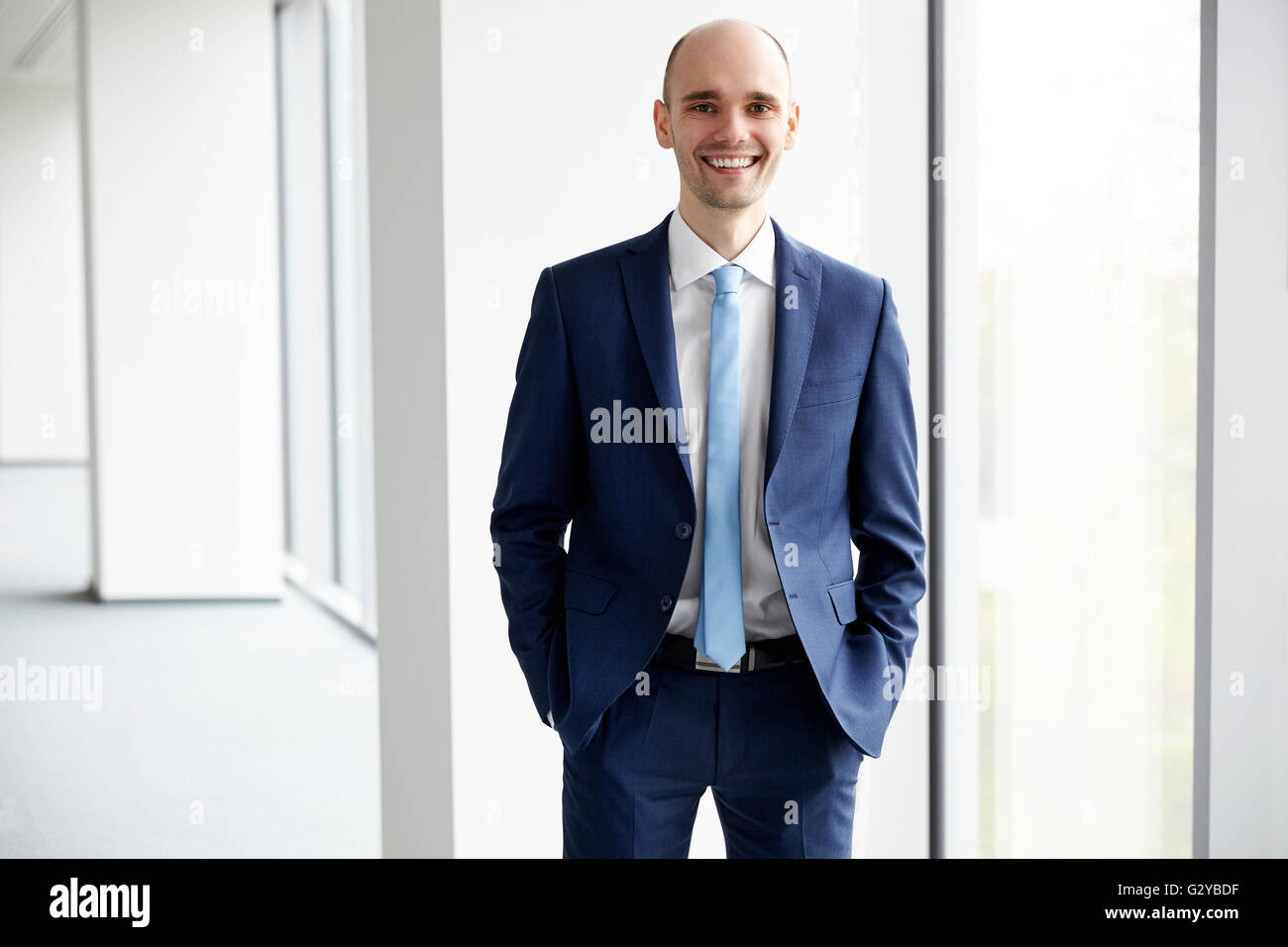 Portrait of young businessman standing dans le bureau. Fond clair. Les mains dans les poches. Banque D'Images