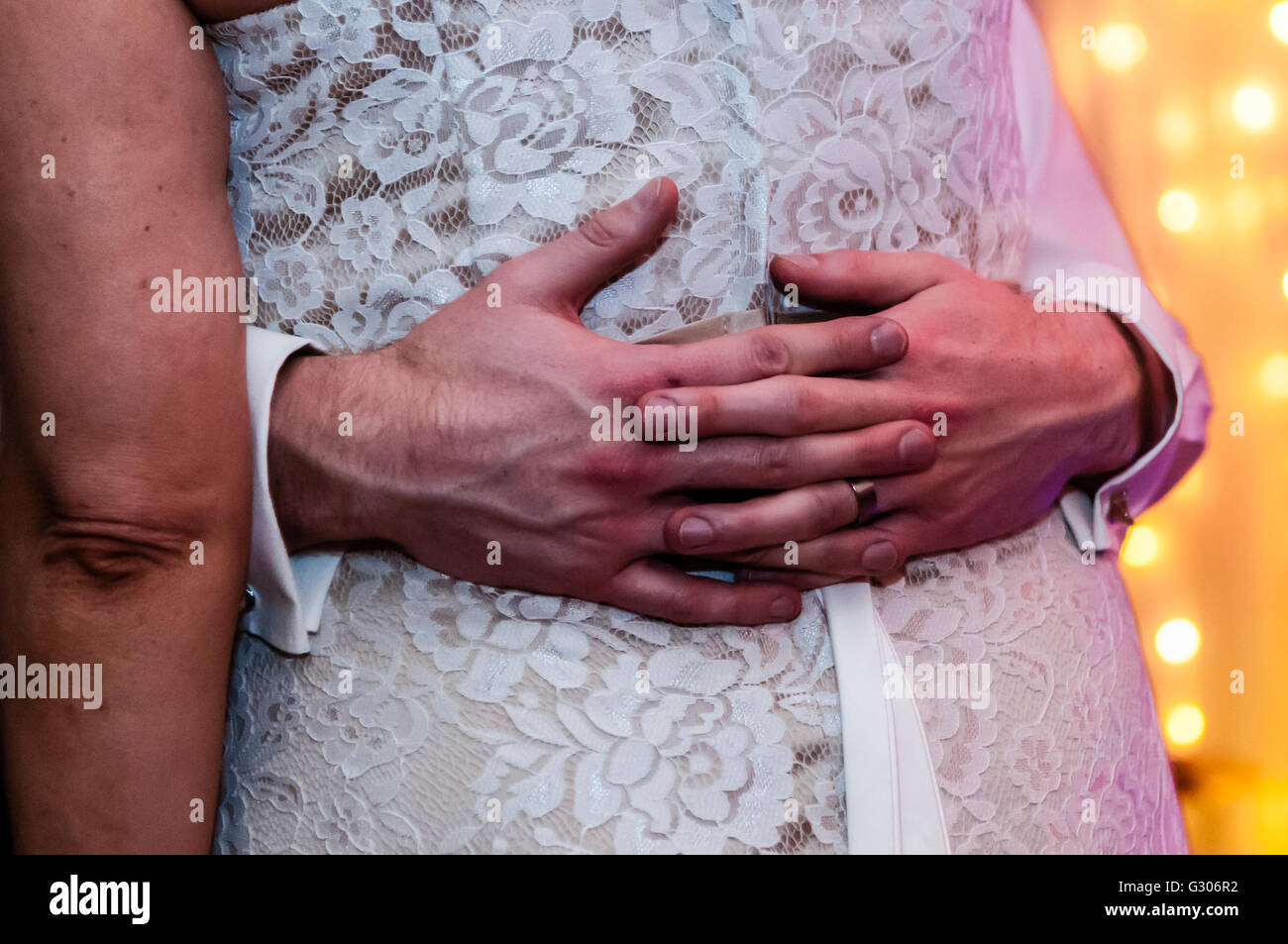 Un groom's les mains et les bras autour de la taille de son épouse au cours de la soirée de danse à un mariage. Banque D'Images