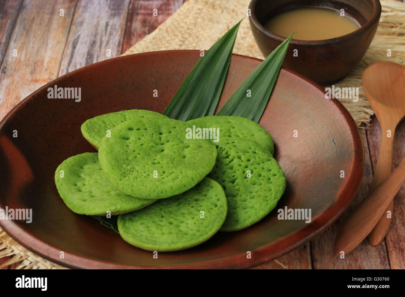 Serabi Pandan. Crêpes Pandanus avec du lait de coco et sucre de palme sauce. Organisées sur la vaisselle en terre cuite traditionnels. Banque D'Images