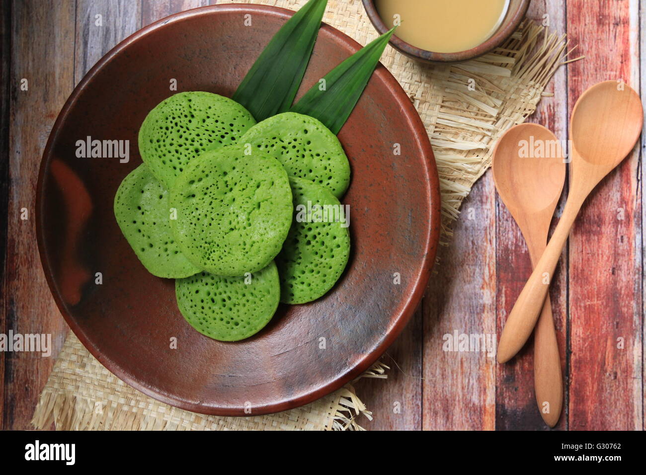 Serabi Pandan. Crêpes Pandanus avec du lait de coco et sucre de palme sauce. Organisées sur la vaisselle en terre cuite traditionnels. Banque D'Images