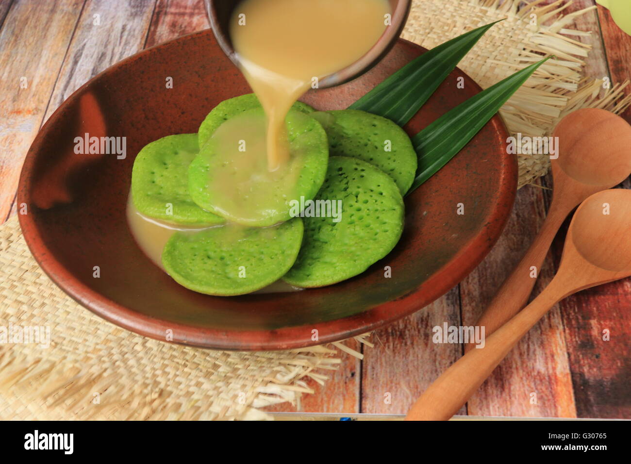 Serabi Pandan. Crêpes Pandanus avec du lait de coco et sucre de palme sauce. Organisées sur la vaisselle en terre cuite traditionnels. Banque D'Images