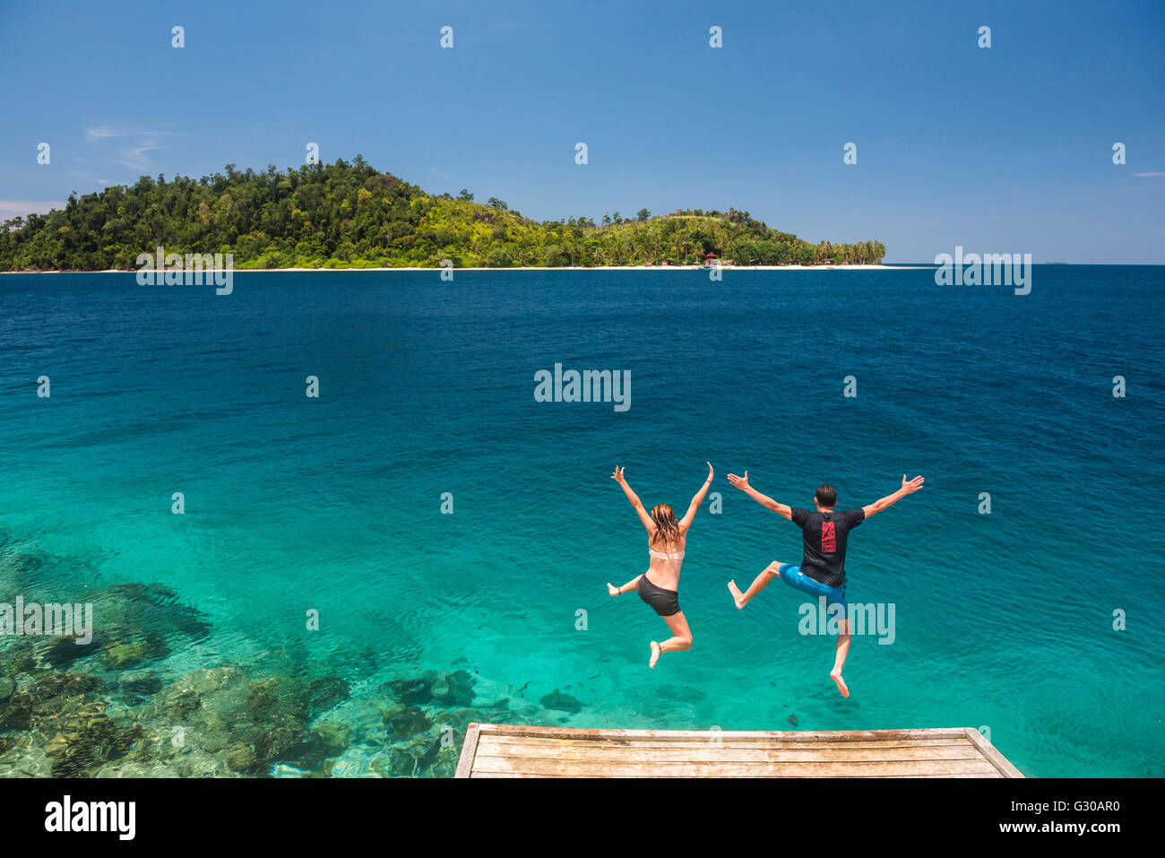 Couple de sauter dans l'océan Pacifique au Twin Beach, une plage de sable blanc tropicales près de Padang à l'Ouest de Sumatra, Indonésie Banque D'Images