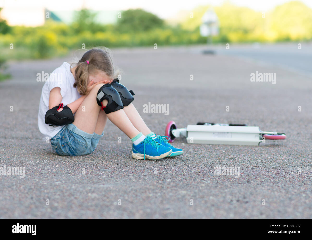 Petite fille est tombée de la trottinette dans la rue. Banque D'Images