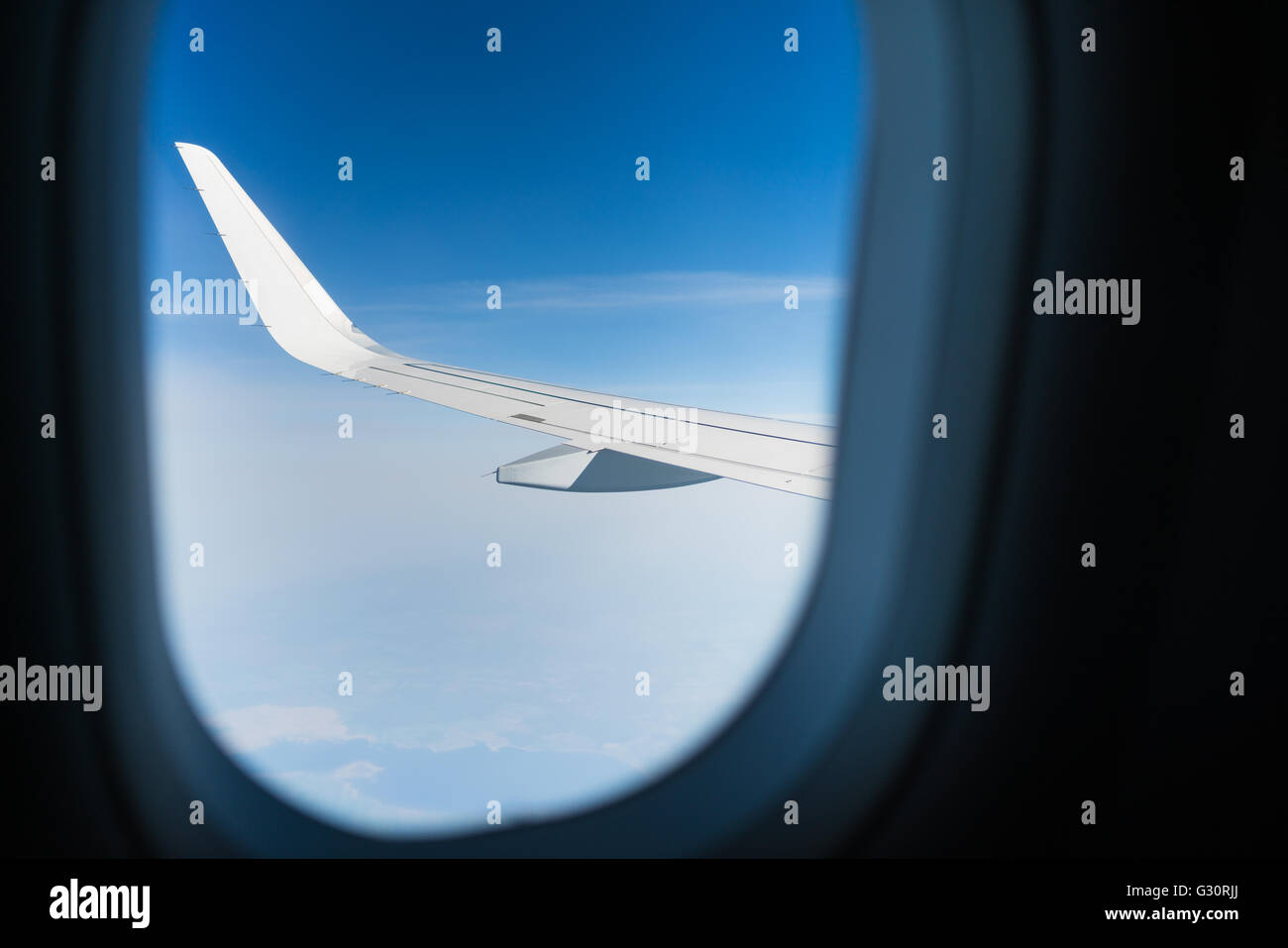 Vue À TRAVERS UNE FENÊTRE D'UN AVION DE PASSAGERS AVEC L'AILE EN VUE ET UN CIEL NUAGEUX BLEU AVEC LA TERRE CI-DESSOUS Banque D'Images