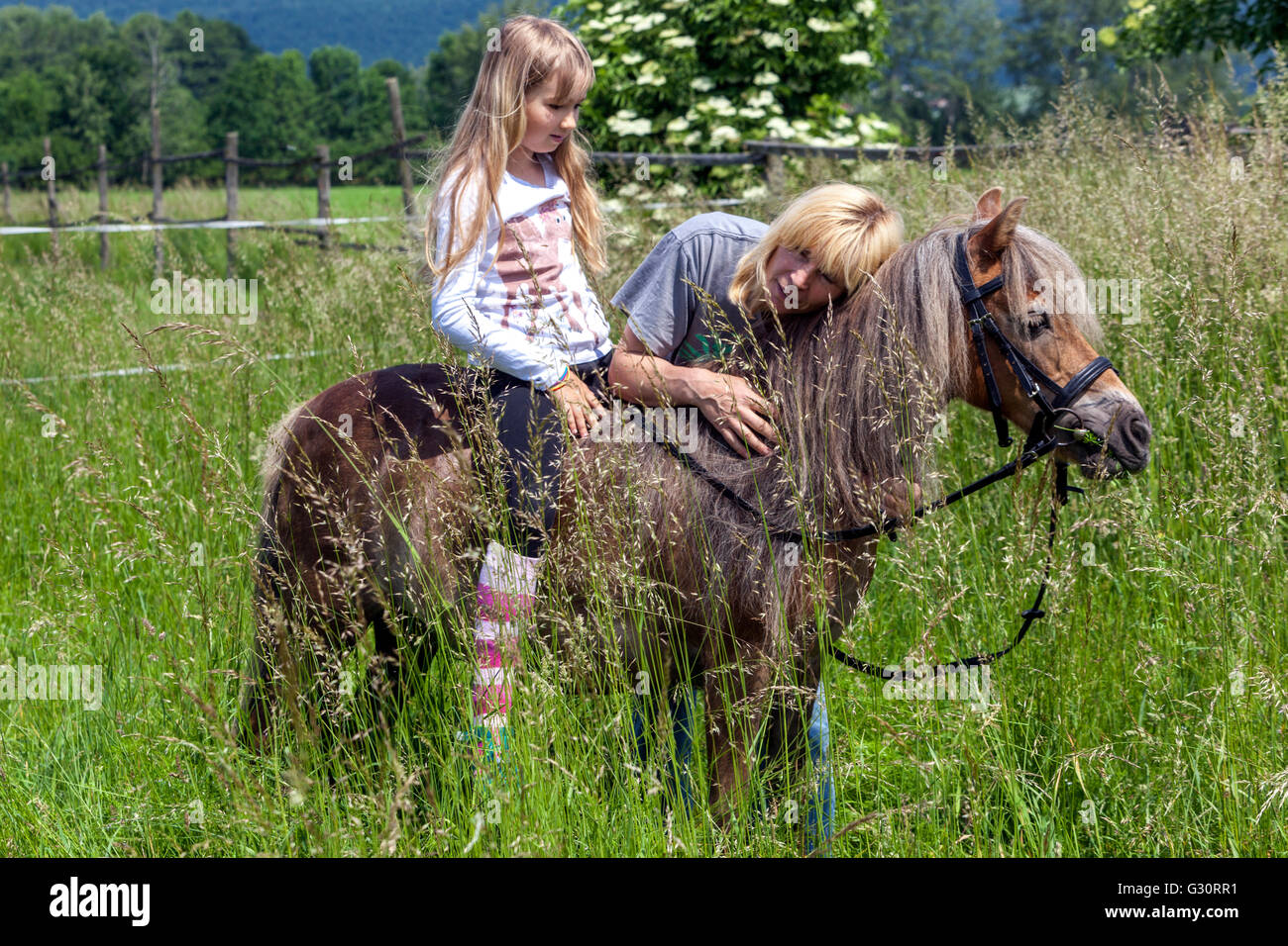Petite fille équitation poney, fille cheval et femme dans un pré herbacé, enfant sur poney Banque D'Images