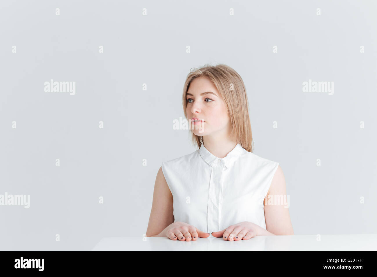 Belle blonde femme assise à la table et à l'écart isolé sur fond blanc Banque D'Images