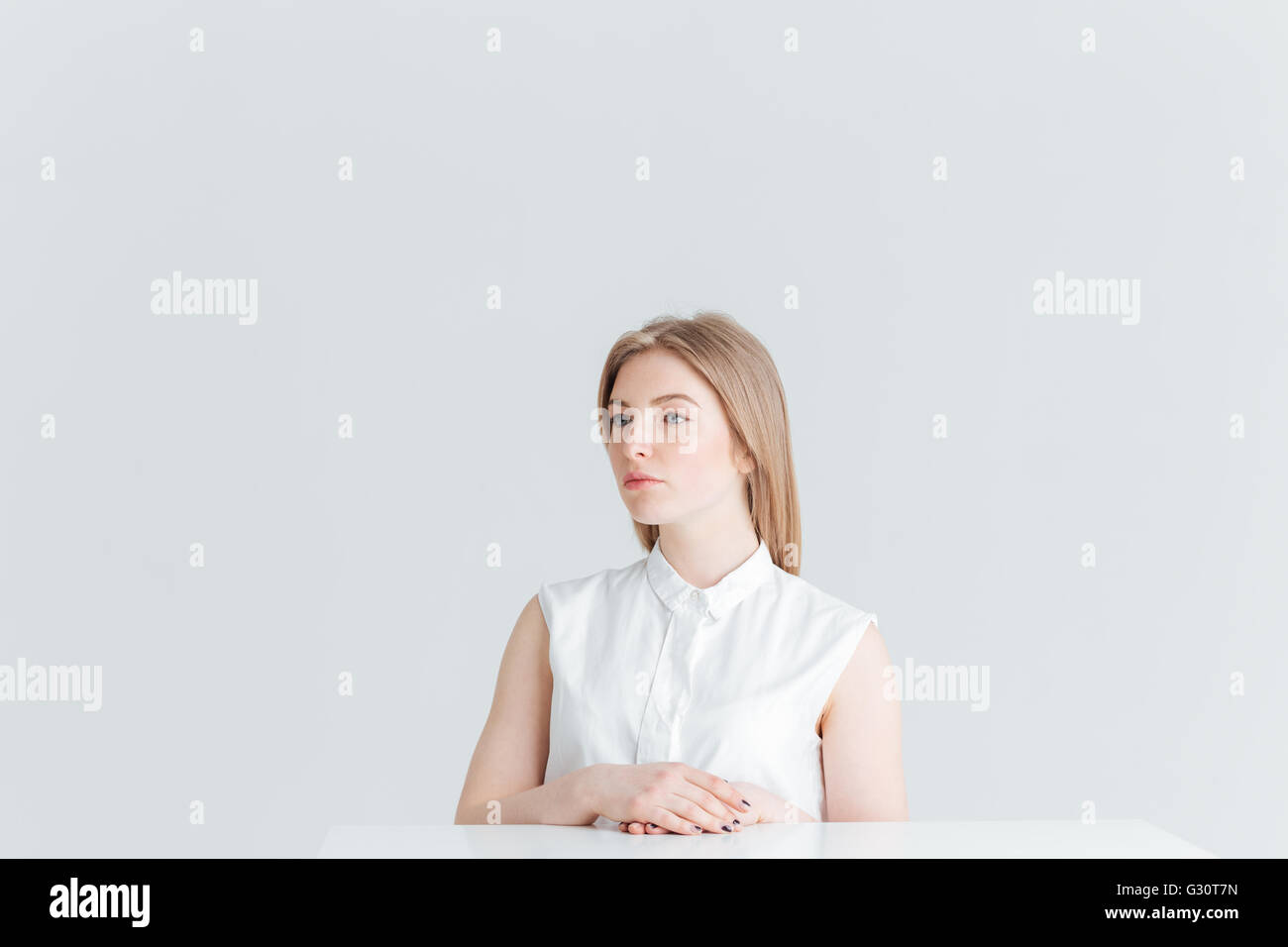 Belle femme blonde assise à la table isolé sur un fond blanc et à l'écart Banque D'Images