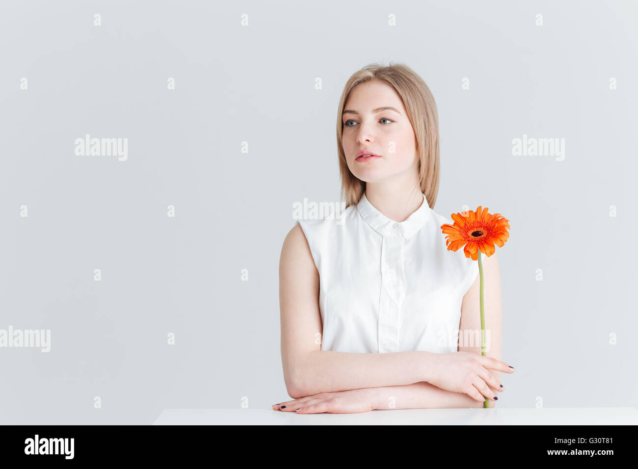 Charmante femme assise à la table et holding flower isolé sur fond blanc Banque D'Images