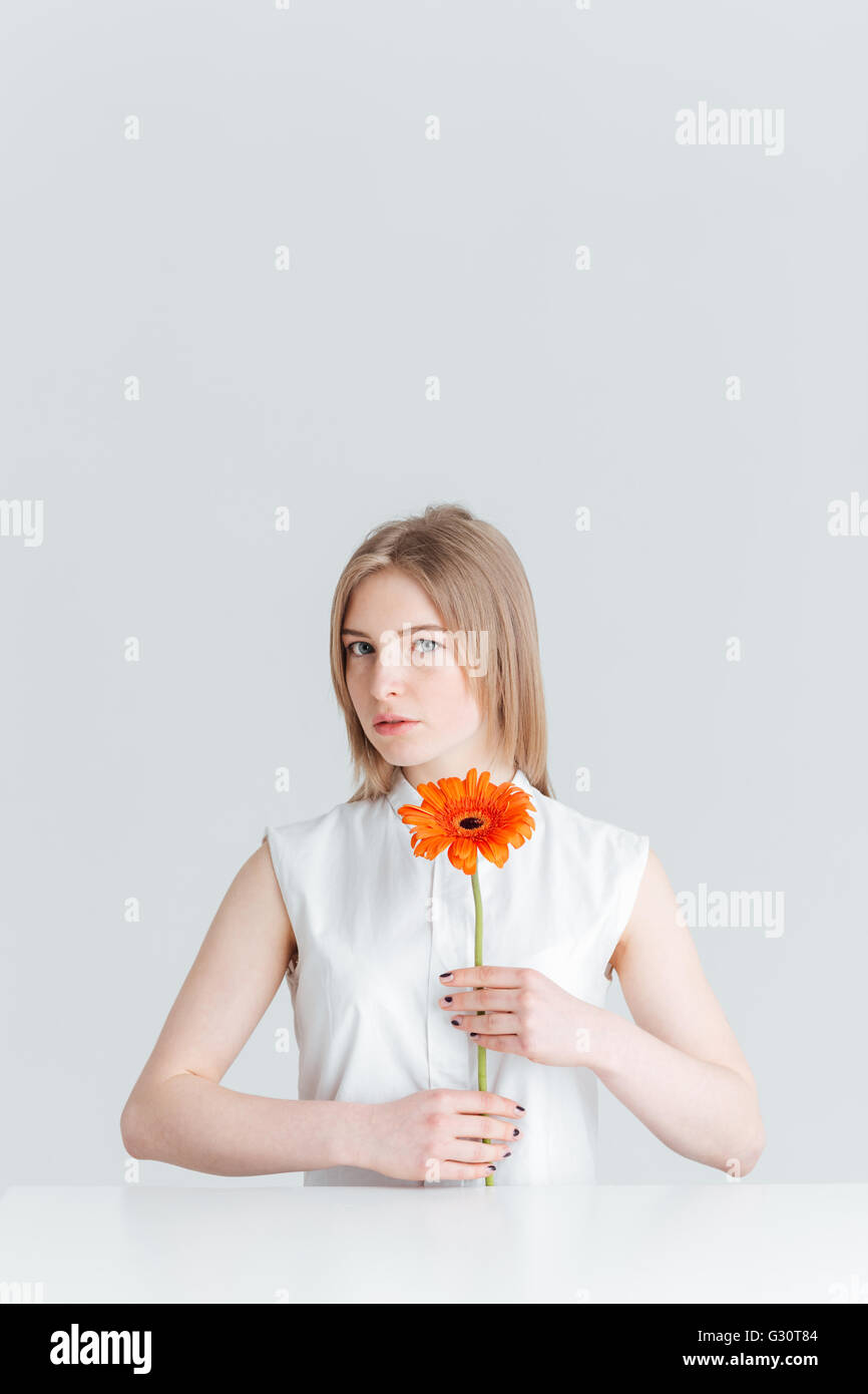 Portrait of attractive blonde femme assise à la table et holding flower isolé sur fond blanc Banque D'Images