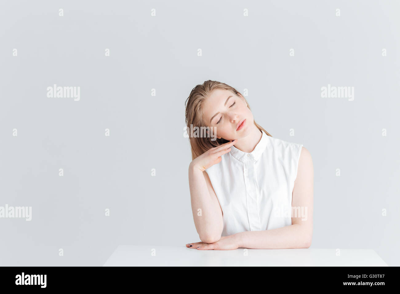 Belle femme assise à la table avec les yeux fermé isolé sur fond blanc Banque D'Images