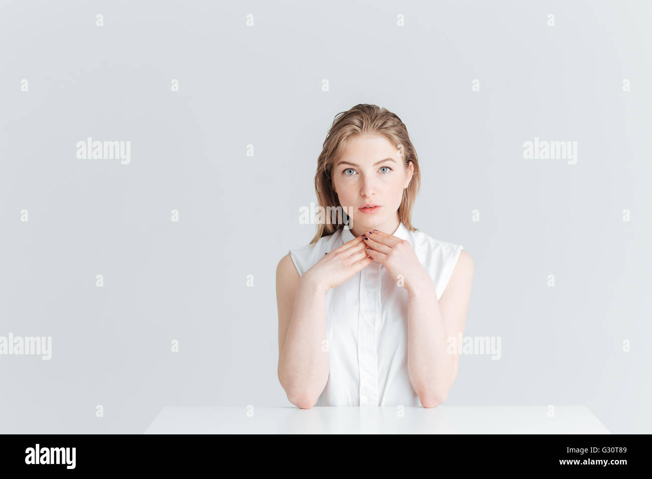 Belle femme assise à la table et à la caméra à isolé sur fond blanc Banque D'Images