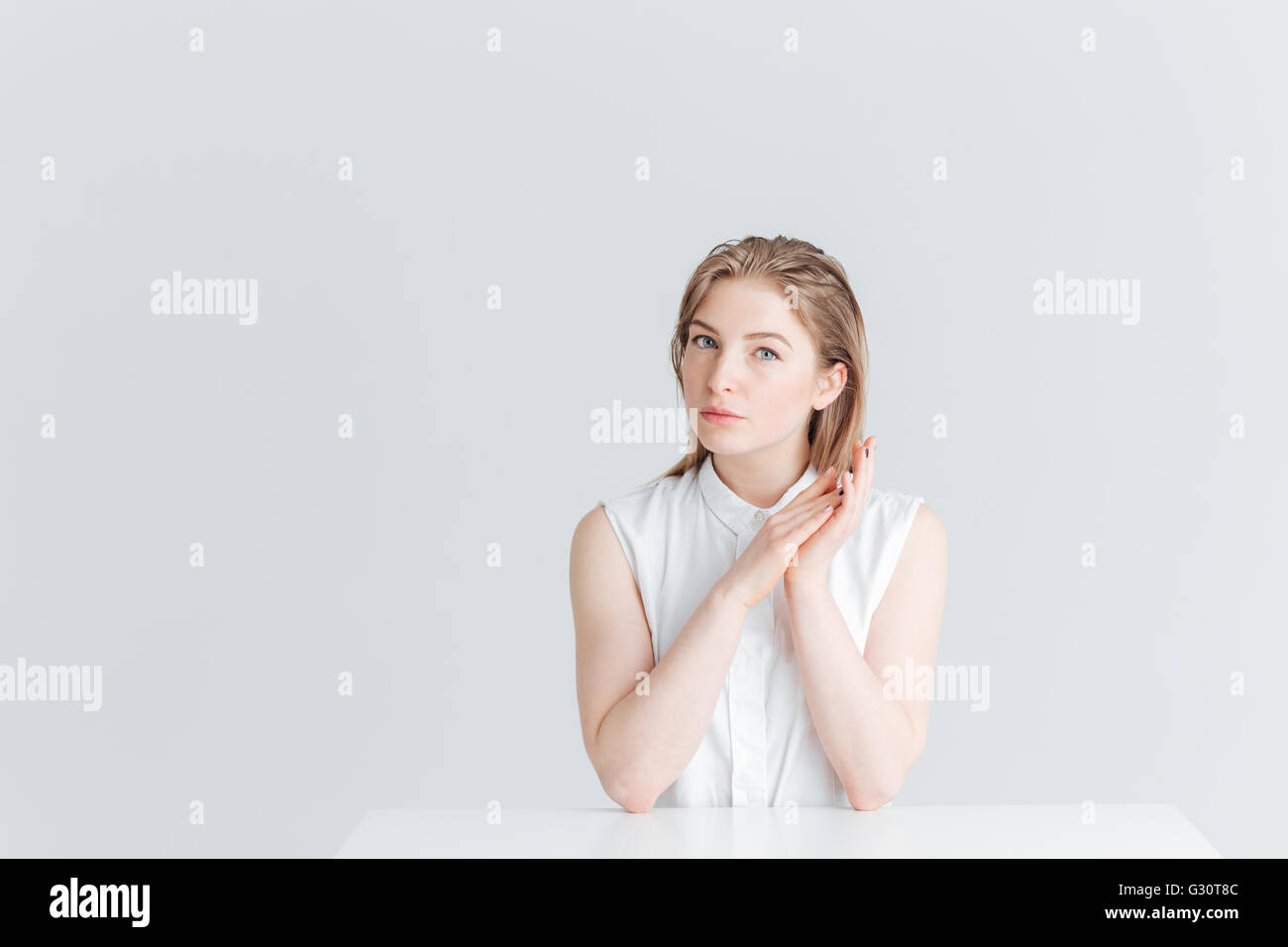 Charmante jeune femme assise à la table et à la caméra à isolé sur fond blanc Banque D'Images