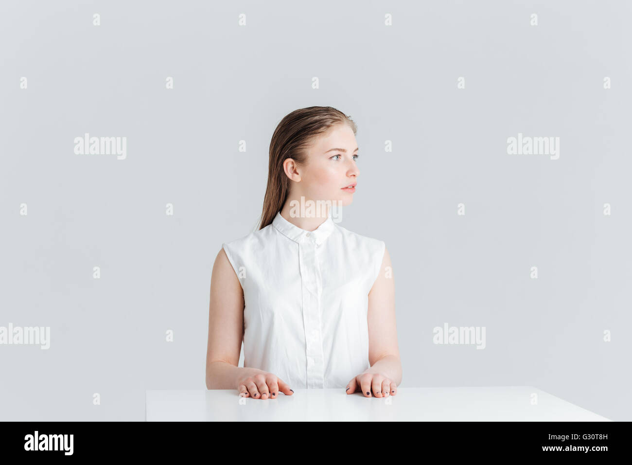 Belle femme assise à la table et à l'écart isolé sur fond blanc Banque D'Images