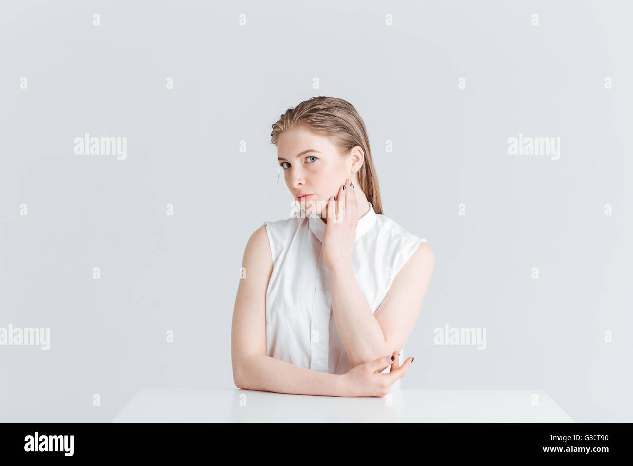 Portrait de beauté d'une belle femme assise à la table et à la caméra à isolé sur fond blanc Banque D'Images
