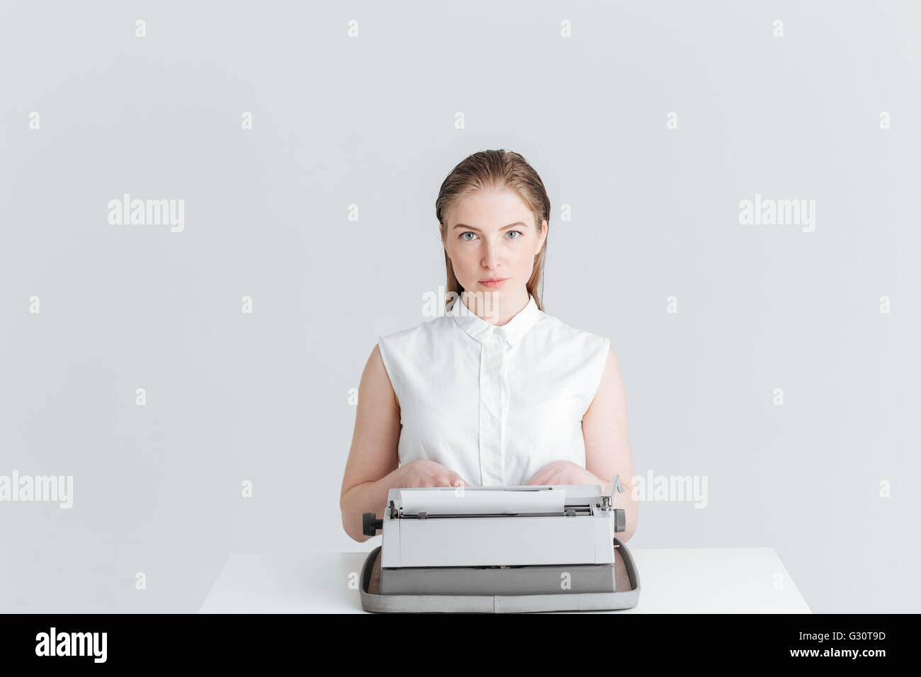 Jeune femme assise à la table et en tapant sur la machine rétro isolé sur fond blanc Banque D'Images