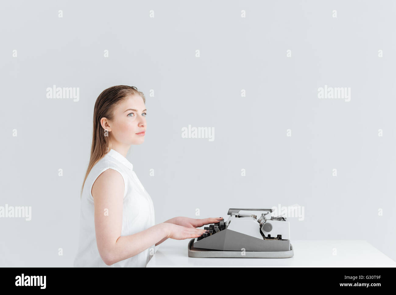 Pensive woman typing on retro machine isolé sur un fond blanc Banque D'Images