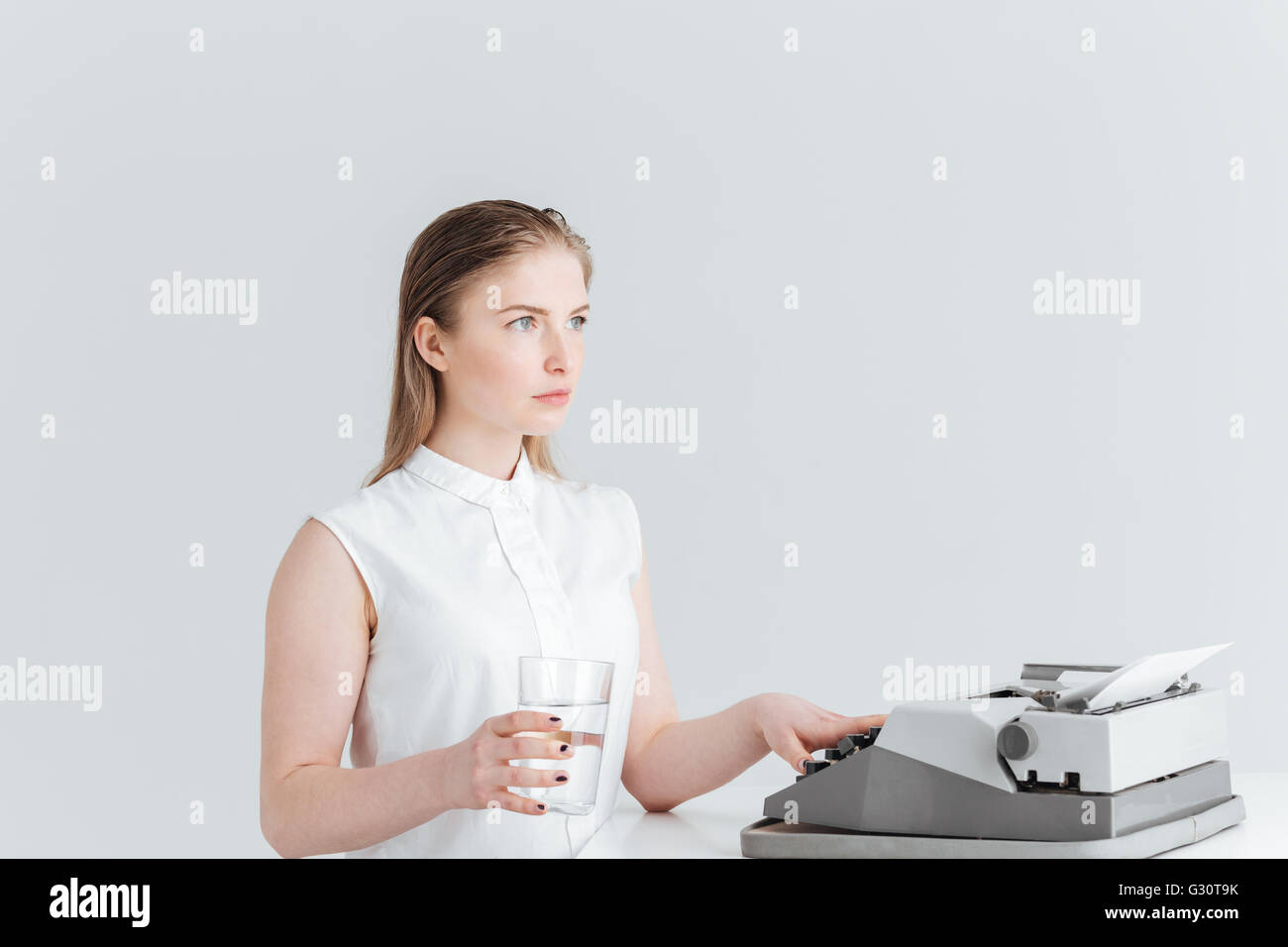 Jeune femme worrking sur machine d'impression rétro et holding glass avec de l'eau isolé sur fond blanc Banque D'Images