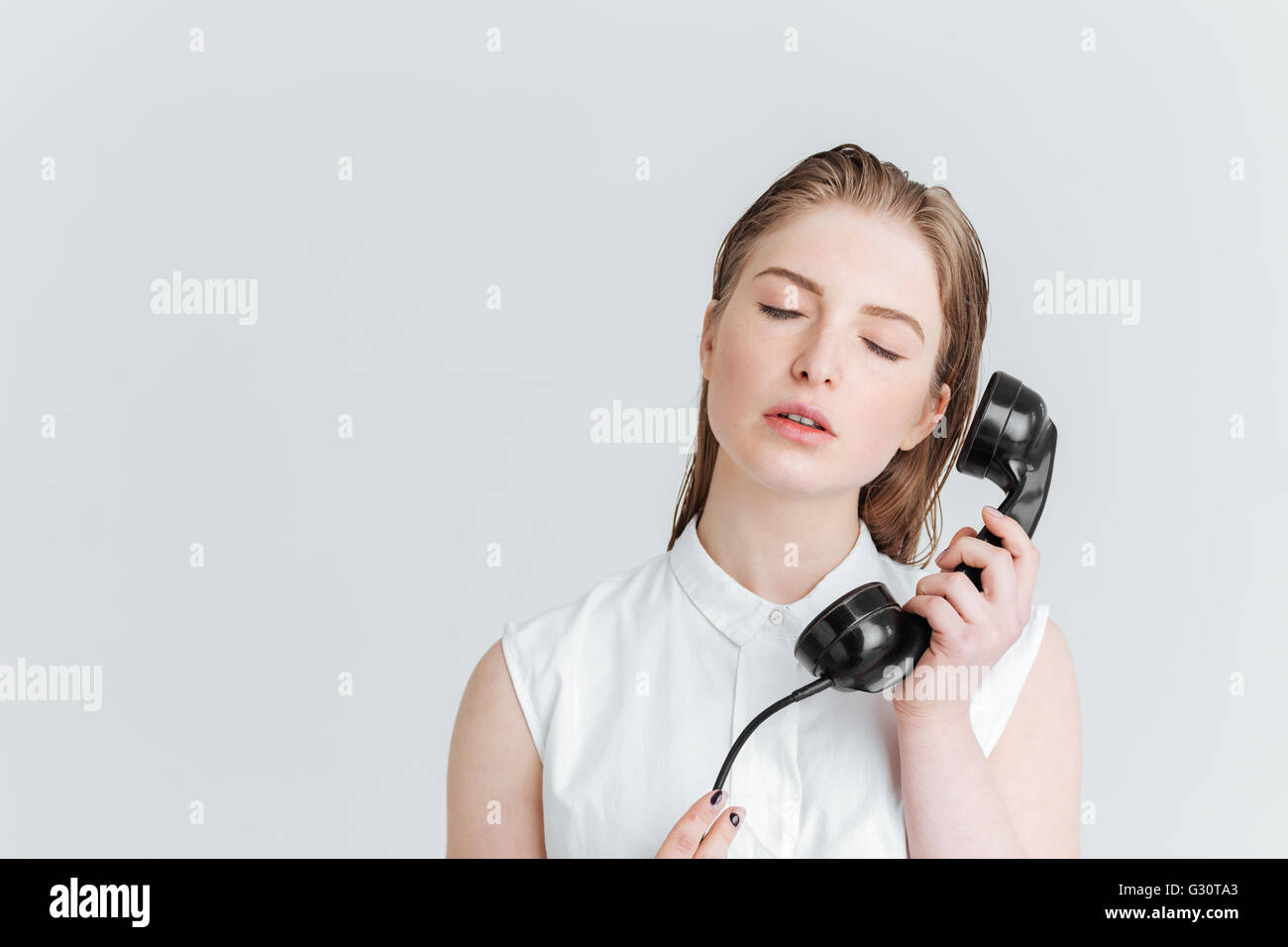 Relaxed woman with closed eyes holding retro phone tube isolé sur fond blanc Banque D'Images
