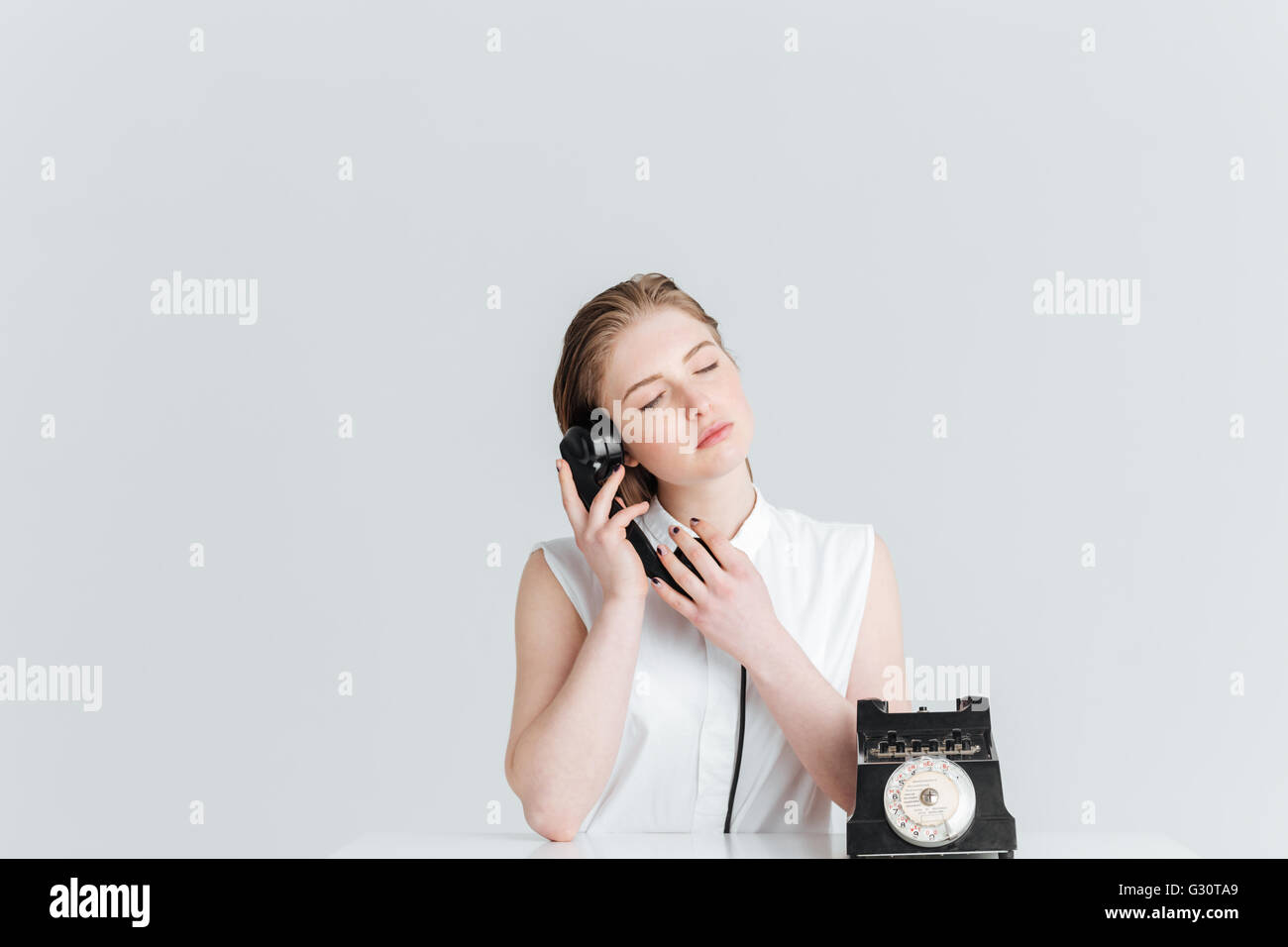 Relaxed woman with closed eyes parlant au retro phone isolé sur fond blanc Banque D'Images