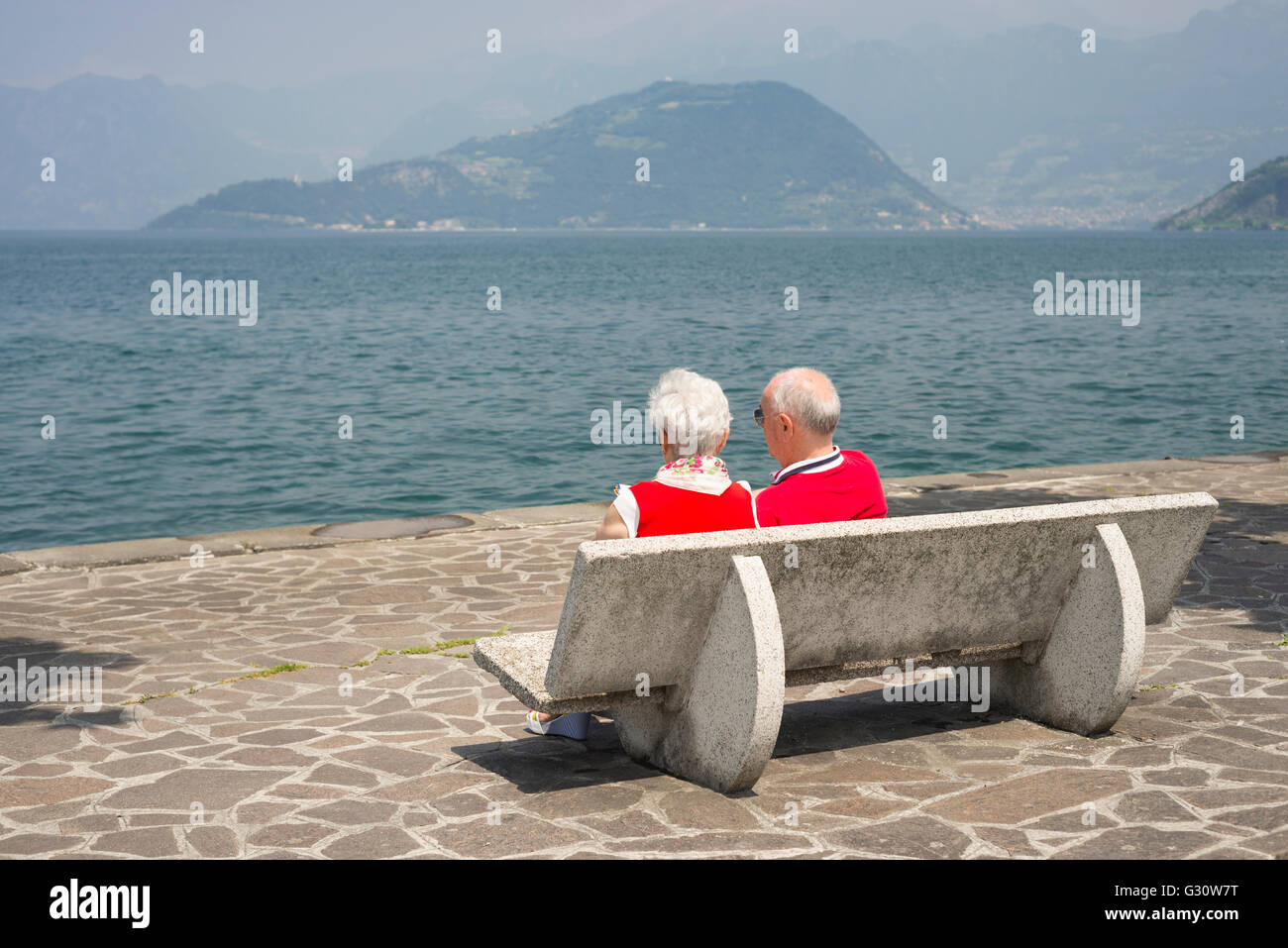Couple de personnes âgées assis au soleil sur banc de parc en Iseo sur la rive du lac d'Iseo, Lombardie, Italie Banque D'Images