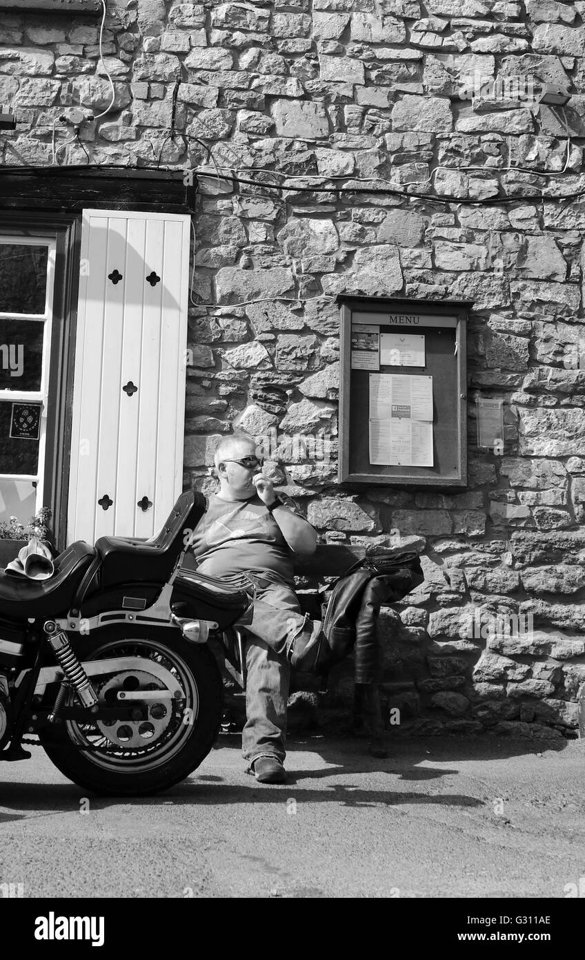 2016 juin - un gars mûr et sa grosse Harley Davidson moto prenant une pause dans le soleil par un traditionnel Pub de campagne anglais Banque D'Images