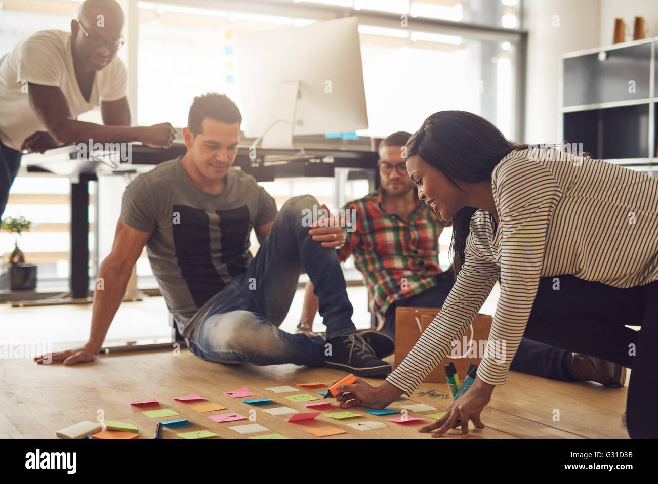 Groupe de quatre employés séance autour de diverses notes adhésives de couleur sur plancher de petit bureau Banque D'Images