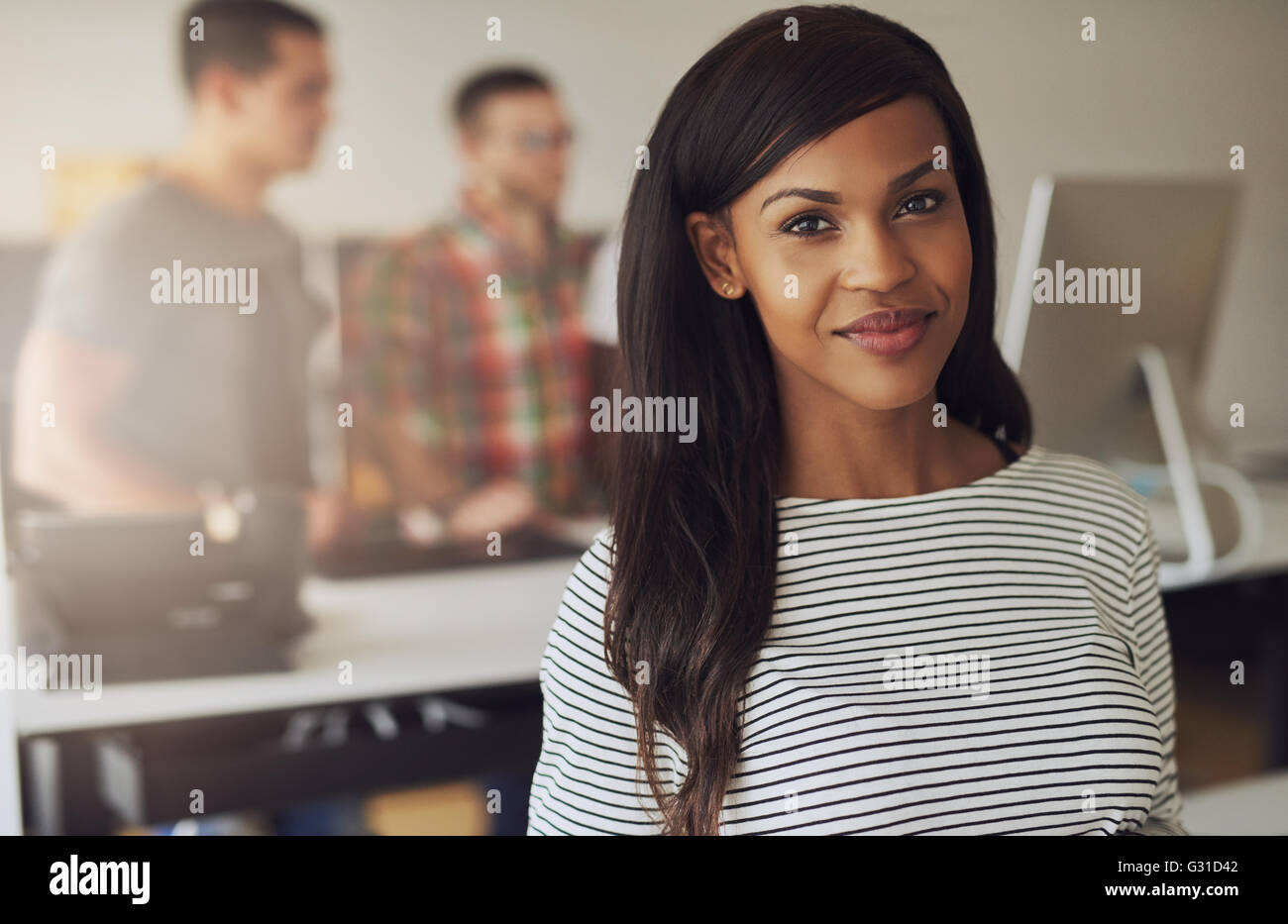 Belle femme seule propriétaire de l'entreprise portant Chemisier rayé noir et blanc avec deux employés sur l'ordinateur en arrière-plan Banque D'Images