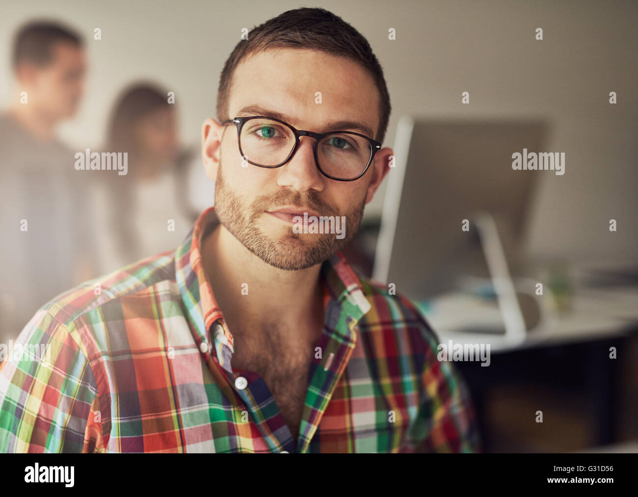 Close up of handsome travailleur barbu portant des lunettes et de flanelle en petit bureau avec d'autres membres du personnel en arrière-plan Banque D'Images