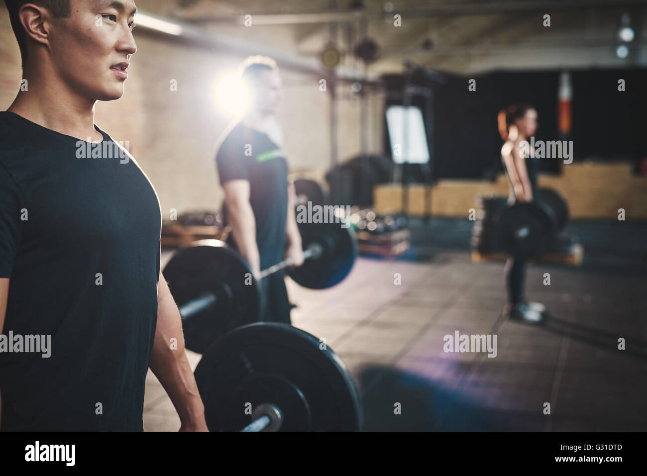 Mettre en place des barres de levage de jeune homme à l'accent, s'entraîner dans un gymnase avec d'autres personnes Banque D'Images